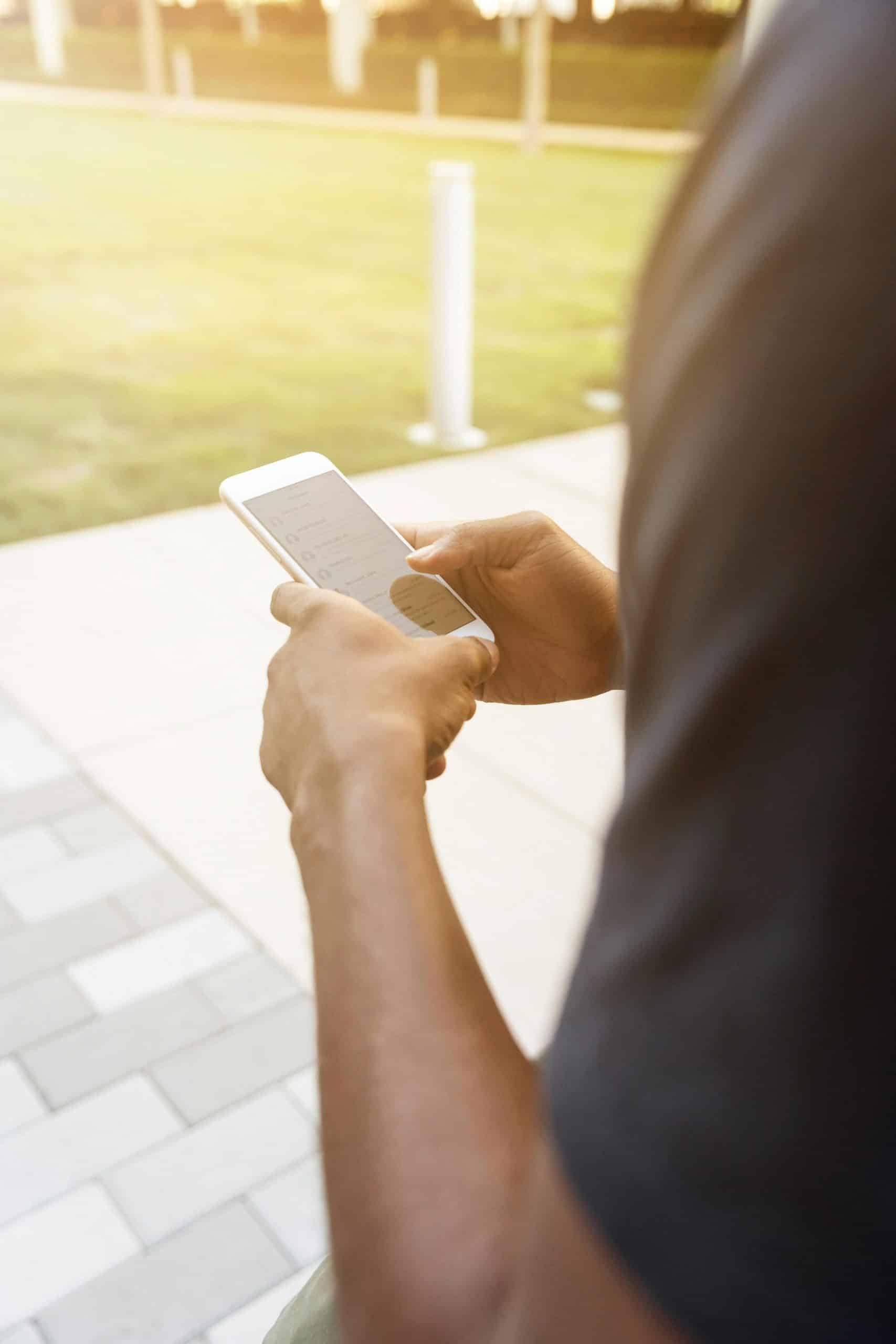 A close-up view of a person texting on a smartphone in a sunlit outdoor setting.